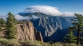 Stunning panoramic view of rugged mountain cliffs with dramatic cloud formations hovering above a forested landscape on a bright, Royalty Free Stock Photo