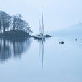 Stunning peaceful landscape image of misty Spring morning over Windermere in Lake District and distant misty peaks