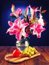 Stunning pink lily bouquet in glass vase on a wooden table and fresh fruit. Still life. Dark background Royalty Free Stock Photo