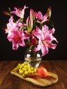 Stunning pink lily bouquet in glass vase on a wooden table and fresh fruit. Still life. Dark background Royalty Free Stock Photo