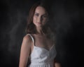 Stunning portrait of a sexy young brunette girl in a white dress sitting on a high chair on a black background. Low key. Beauty Royalty Free Stock Photo