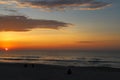 A stunning red and yellow sunrise over the vast ocean with waves rolling into the shore and people on the beach and clouds Royalty Free Stock Photo