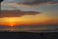 A stunning red and yellow sunrise over the vast ocean with waves rolling into the shore and people on the beach and clouds Royalty Free Stock Photo