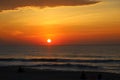 A stunning red and yellow sunrise over the vast ocean with waves rolling into the shore and people on the beach and clouds Royalty Free Stock Photo