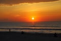 A stunning red and yellow sunrise over the vast ocean with waves rolling into the shore and people on the beach and clouds Royalty Free Stock Photo