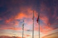 A stunning share of an American flag and two other flags flying on tall flag poles with blue sky and powerful red colored clouds Royalty Free Stock Photo