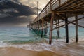 A stunning shot of the Balboa Pier at sunset with powerful clouds, vast blue ocean water and waves crashing into the pier Royalty Free Stock Photo