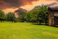 A stunning shot of a brown long cabin surrounded by lush green grass and lush green trees with parked cars and a powerful clouds Royalty Free Stock Photo