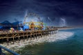 A stunning shot of a colorful Ferris wheel, rollercoaster and carnival games on a long brown wooden pier