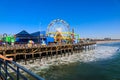 A stunning shot of a colorful Ferris wheel, rollercoaster and carnival games on a long brown wooden pier