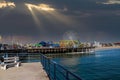 A stunning shot of a colorful Ferris wheel, rollercoaster and carnival games on a long brown wooden pier