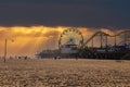 A stunning shot of a Ferris wheel, rollercoaster and colorful carnival games on a long brown wooden pier with silky brown sand