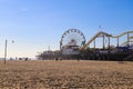 A stunning shot of a Ferris wheel, rollercoaster and colorful carnival games on a long brown wooden pier with silky brown sand