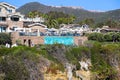 A stunning shot of the hillside at the beach covered with lush green plants and a hotel with umbrellas with palm trees