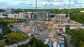 A stunning shot of large tower cranes on dirt covered a construction site surrounded by buildings and lush green trees Royalty Free Stock Photo