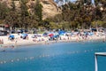 A stunning shot of people relaxing on the sandy beach and playing in the deep blue ocean water surrounded by cliffs