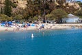 A stunning shot of people relaxing on the sandy beach and playing in the deep blue ocean water surrounded by cliffs