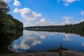 A stunning shot of the still blue waters of the lake with blue sky and clouds reflecting off the water and of lush green trees