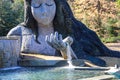 A stunning shot of the waterfall goddess surrounded by lush green trees and plants, bare winter trees with pond and blue sky