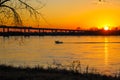 A stunning shot of a white motor boat sailing down the Mississippi river with a gorgeous yellow and red sunset with trees