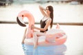 Stunning woman is wearing black bikini sitting in swimming pool with blue water on a pink flamingo mattress Royalty Free Stock Photo