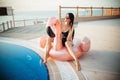 Stunning slim woman is wearing black bikini sitting in swimming pool with blue water on a pink flamingo mattress, summer Royalty Free Stock Photo