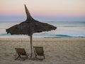 Stunning sunrise with a traditional straw beach umbrella and two deckchairs facing the peaceful Indian Ocean coast, Anakao, Madaga