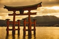 Stunning sunset view of Miyajima Torii gate in the golden water with mountains in the back. This gate is the most famous Torii in