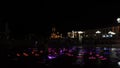 Colorful fountain lit up at night in a city square. A kid are playing