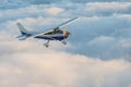 Stunning view of a blue and white little private Cessna airplane browsing the sky over fluffy fairy tale clouds.