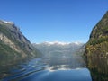 View of Norwegian fjord from rear of boat with snow capped mountains reflected in the ripples of water