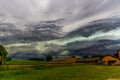 Stunning view of a storm with gray and white clouds above a farm and green meadow