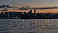 Stunning view of Vancouver skyline with skyscrapers light after sunset with orange colored sky and cargo ship in front.