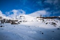 Stunning winter landscape with snow blanketed mountain range and sky lift lines climbing up the slope. Tractor tracks