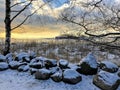 Winter view over the Baltic Sea with snow covered stones on the shore and trees under the sky with sun lighted clouds Royalty Free Stock Photo