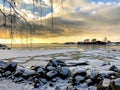 Winter view over the Baltic Sea with ice floes and snowy stones and building with trees on the background under the cloudy sky Royalty Free Stock Photo