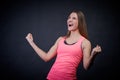 Stunning woman in sports uniform on an isolated black background keeps her fists from happiness, showing victory