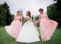 Stunning young bride and bridesmaids in pink dresses stand with wedding bouquets in the park Royalty Free Stock Photo