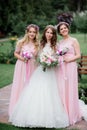 Stunning young bride and bridesmaids in pink dresses stand with wedding bouquets in the park Royalty Free Stock Photo