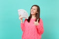 Stunning young woman in knitted pink sweater showing thumb up, hold in hand lots bunch of dollars banknotes, cash money