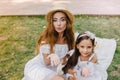 Stunning young woman and pretty girl sharing love with world posing for photo on picnic. Two amazing sisters in similar