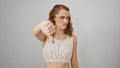 Stunning young woman, standing isolated against a white background, portrays a negative thumbs down gesture. her angry countenance