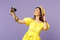 Stunning young woman in yellow dress, summer hat doing selfie on retro vintage photo camera isolated on pastel violet Royalty Free Stock Photo