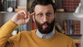 Stupid. Irritated bearded man in glasses in office or apartment room looks at camera and twirls his finger at his temple