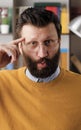 Stupid. Irritated bearded man in glasses in office or apartment room looks at camera and twirls his finger at his temple