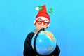 A stupid and surprised boy in a Christmas hat and funny glasses looks at the globe Royalty Free Stock Photo