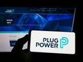 Person holding smartphone with logo of US hydrogen fuel cell company Plug Power Inc. on screen in front of website.