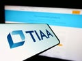 Mobile phone with logo of American financial services company TIAA on screen in front of business website.