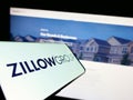 Mobile phone with logo of American real estate company Zillow Group Inc. on screen in front of website.