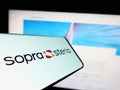 Mobile phone with logo of French company Sopra Steria Group SA on screen in front of business website.
